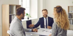 Realtor in a suit discussing commissions with a couple in a modern office setting.