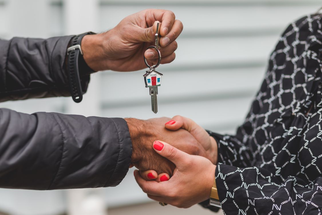 A firm, professional handshake between a homeowner and a realtor inside a bright, modern living room, symbolizing a successful listing agreement.