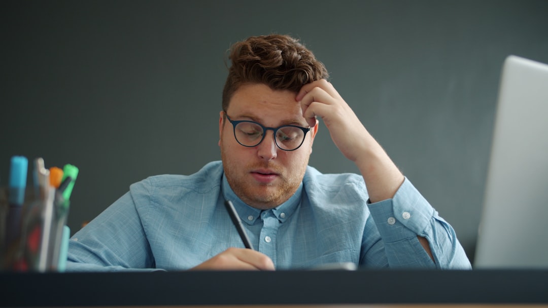 A person looking concerned while reviewing complex information on a laptop, with architectural blueprints on the table, representing the stress of property deal complications.