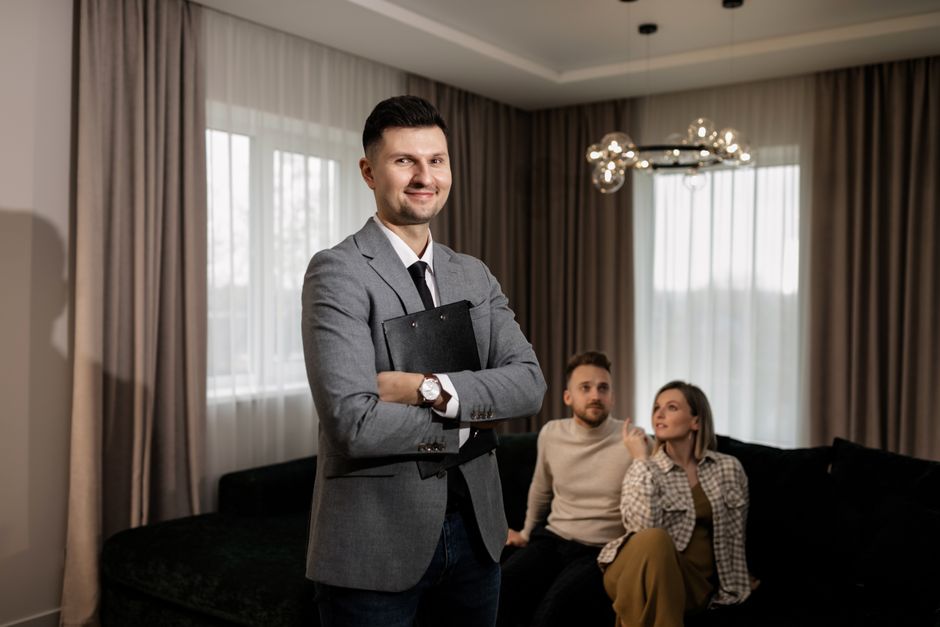 A professional real estate agent discusses paperwork with happy clients in a bright, modern living room, representing a successful and positive home selling experience.