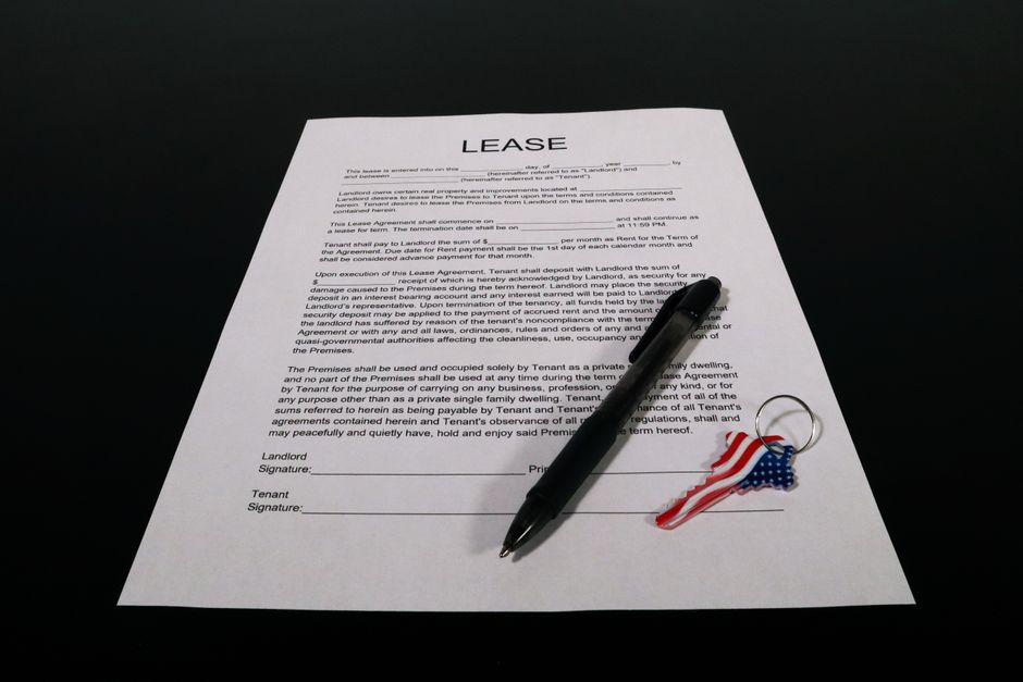A real estate commission agreement and a pen laid out on a modern wooden table next to a set of house keys, representing a property transaction.