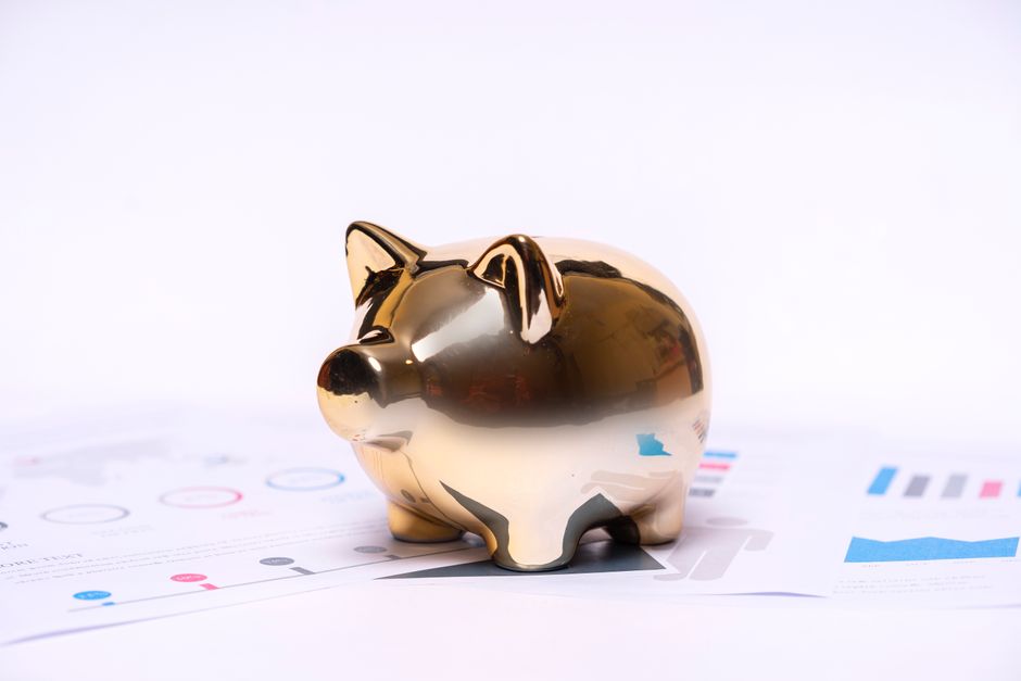 A set of house keys rests next to a white ceramic piggy bank on a clean wooden table, symbolizing the financial savings from a low-commission home sale.